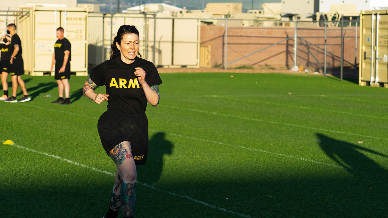 Woman in Army t shirt runs across astroturf field